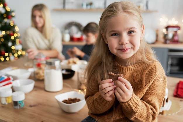 Free Photo cute girl eating homemade cookie while sitting on table