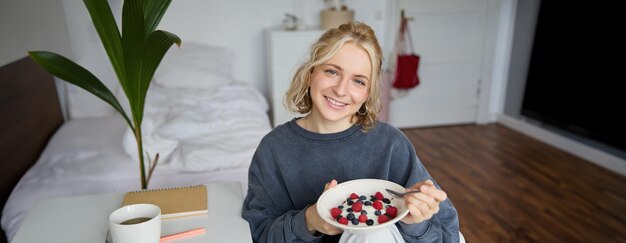 Cute girl eats breakfast and drinks tea in her room makes herself healthy lunch in bowl sits in