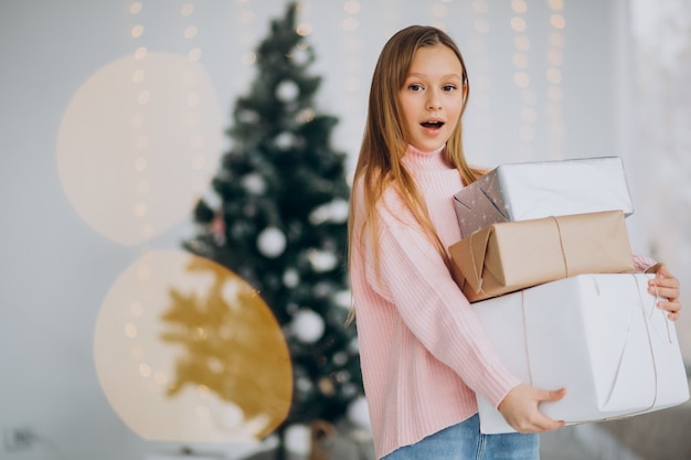 Cute girl holding christmas presents by christmas tree