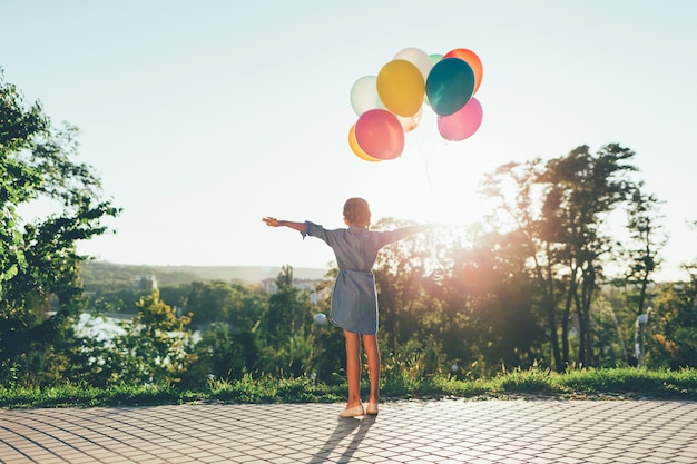 Cute girl holding colorful balloons in the city park