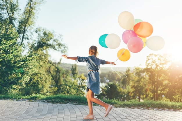 Free photo cute girl holding colorful balloons in the city park