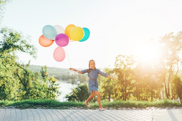 Cute girl holding colorful balloons in the city park