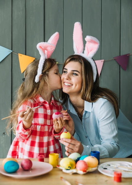 Free Photo cute girl kissing mother on cheek while painting eggs for easter 