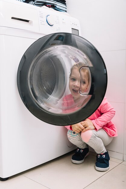 Cute girl looking through washing machine door