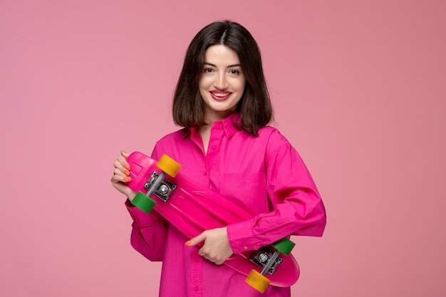 Cute girl lovely young brunette girl in pink shirt with red lipstick holding a bright skateboard