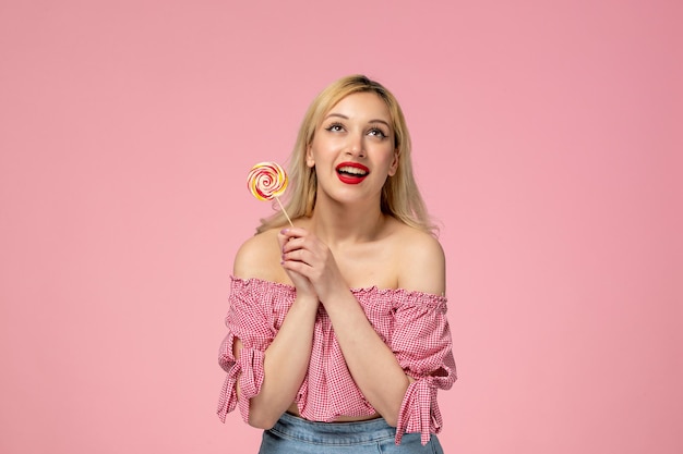 Cute girl lovely young lady with red lipstick in pink blouse holding pink lollipop acting cute