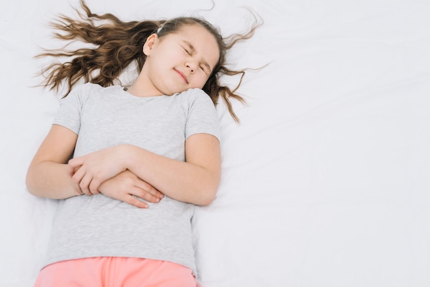 Free photo cute girl lying on white bed suffering from stomach ache