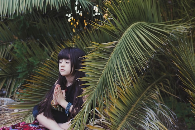 Free photo cute girl meditating near palm