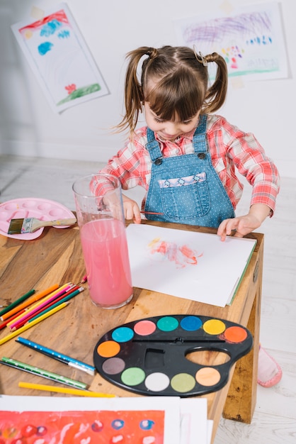 Free photo cute girl painting with aquarelle on paper at table