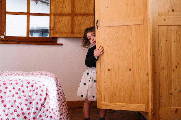 Free photo cute girl peeking from wooden cupboard