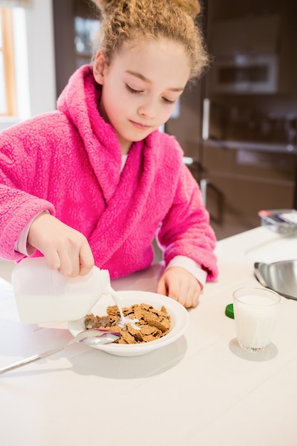 Free photo cute girl pouring milk in cornflakes in kitchen