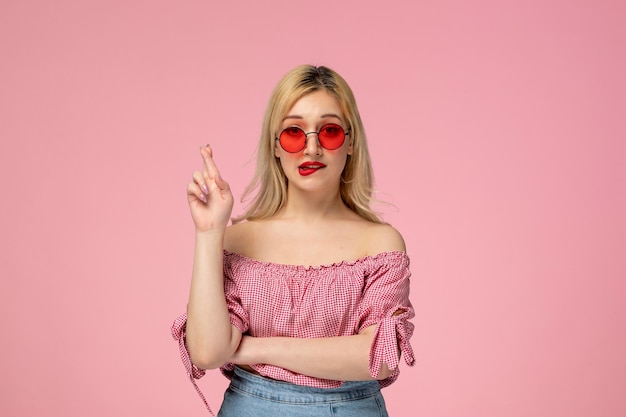 Cute girl pretty blonde lady wearing red glasses in pink shirt crossing fingers and biting lips