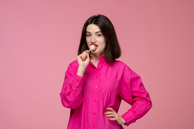 Free photo cute girl pretty young beautiful brunette girl in pink shirt licking a lollipop