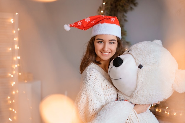 Free photo cute girl in santa hat holding a toy bear