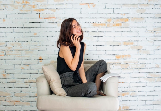 Cute girl sitting on armchair and talking with the phone High quality photo