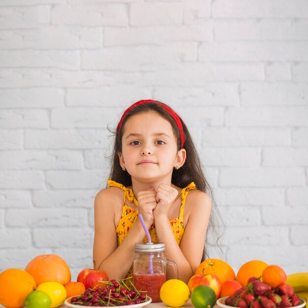 Cute girl standing against white wall with colorful fruits