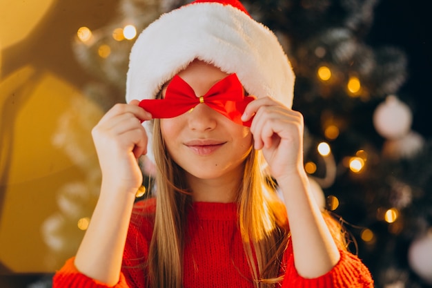 Free photo cute girl teenager in red santa hat by christmas tree