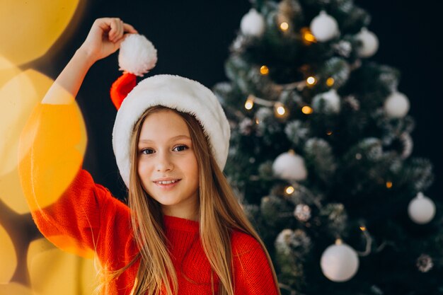 Cute girl teenager in red santa hat by christmas tree