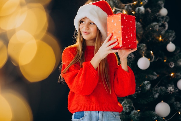 Cute girl teenager in red santa hat by christmas tree