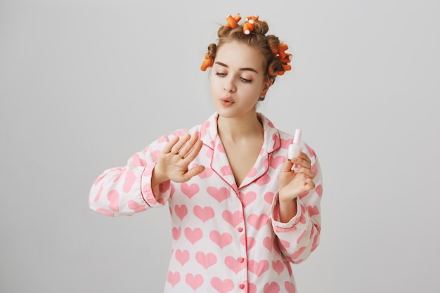 Free photo cute girl with hair curlers in hair and pyjama, polish nails