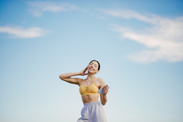 Cute girl with phone training on blue sky