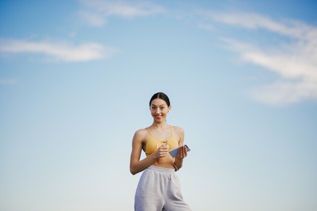 Cute girl with phone training on blue sky