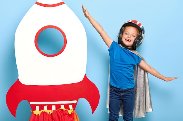 Cute happy female child plays astronaut, wears flying helmet and cape