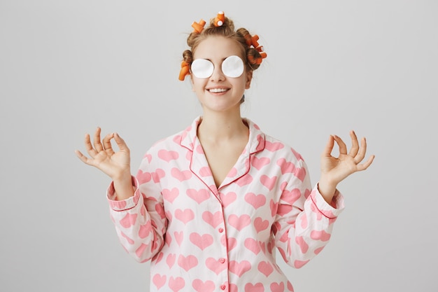 Free Photo cute happy girl in nightwear and hair curlers wipe-off makeup with cotton pads