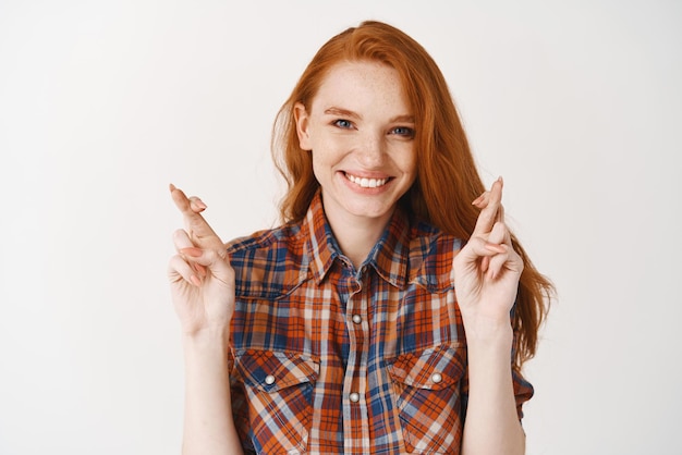 Free photo cute hopeful girl with ginger hair and freckles making a wish smiling and standing with crossed fingers for good luck