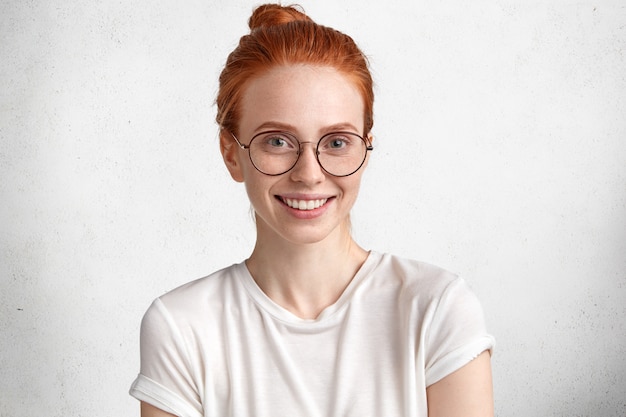 Free photo cute intelligent red haired female student in round spectacles, rejoices successfully passed exam in foreign languages