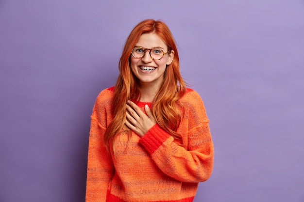 Free photo cute joyful woman feels thankful for hearing pleasant compliment smiles broadly looks gladfully dressed in casual jumper.