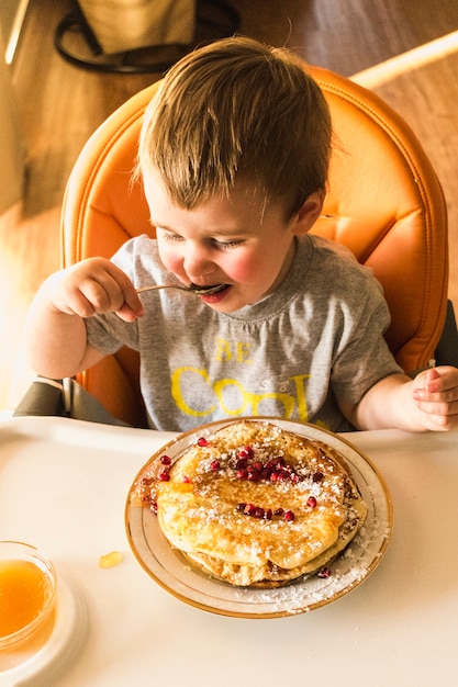 Cute little baby eating pancake on plate over the high chair