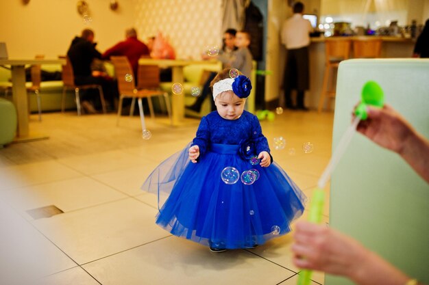 Cute little baby girl at blue dress play with soap bubbles 1 year birthday day