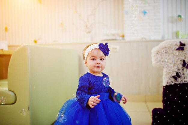 Cute little baby girl at blue dress play with soap bubbles 1 year birthday day