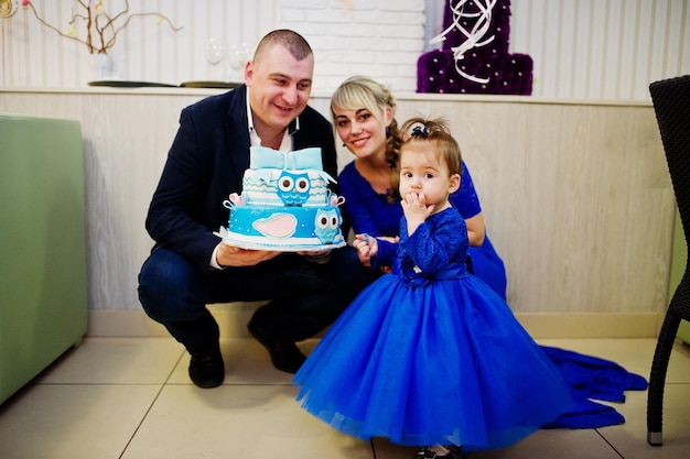 Cute little baby girl at blue dress with 1 year birthday cake father and mother