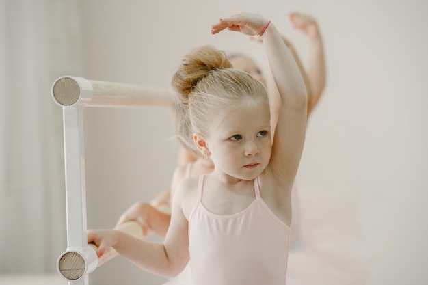 Cute little ballerinas in pink ballet costume. Children in a pointe shoes is dancing in the room. Kid in dance class.