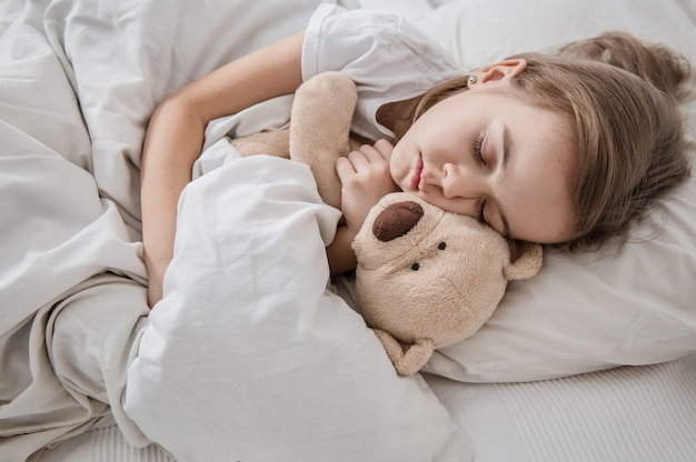 Cute little girl in bed with soft toy.