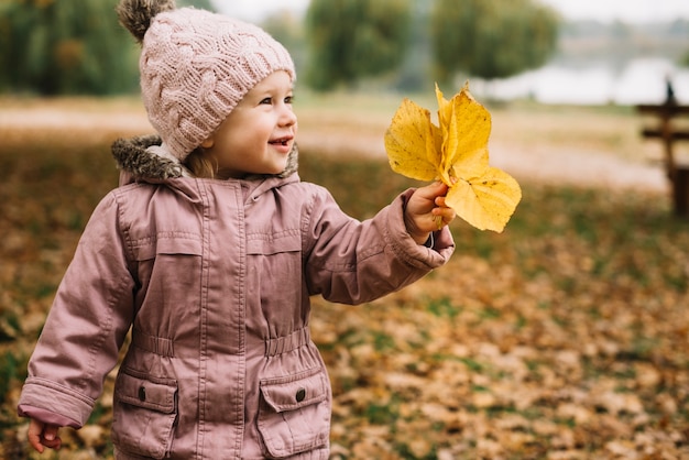 Cute little girl grabbing yellow leaves in autumn park