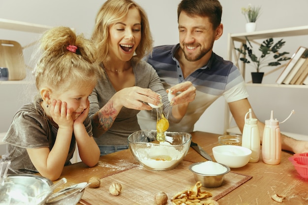 Free photo cute little girl and her beautiful parents preparing the dough for the cake in kitchen at home. family lifestyle concept