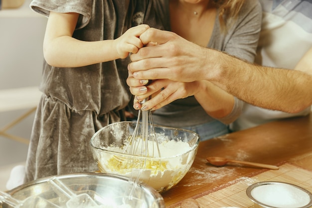 Cute little girl and her beautiful parents preparing the dough for the cake in kitchen at home. Family lifestyle concept