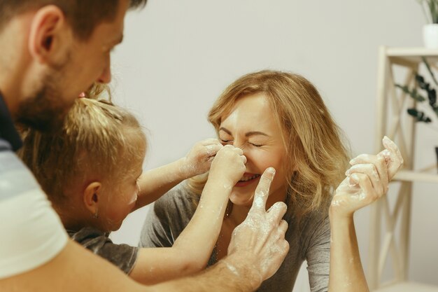 Cute little girl and her beautiful parents preparing the dough for the cake in kitchen at home