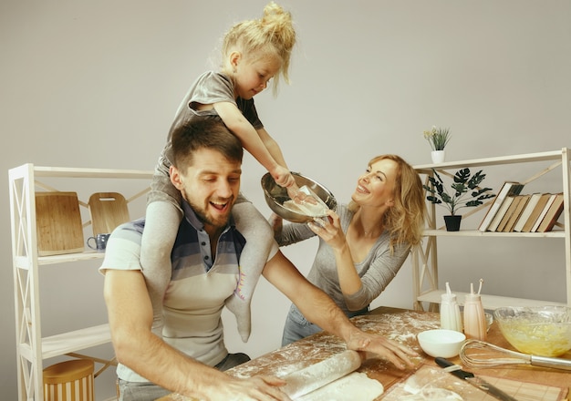 Cute little girl and her beautiful parents preparing the dough for the cake in kitchen at home.