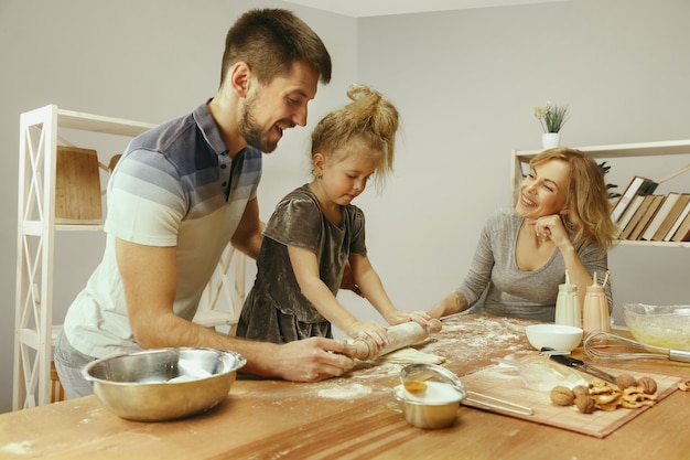 Free Photo cute little girl and her beautiful parents preparing the dough for the cake in kitchen at home.