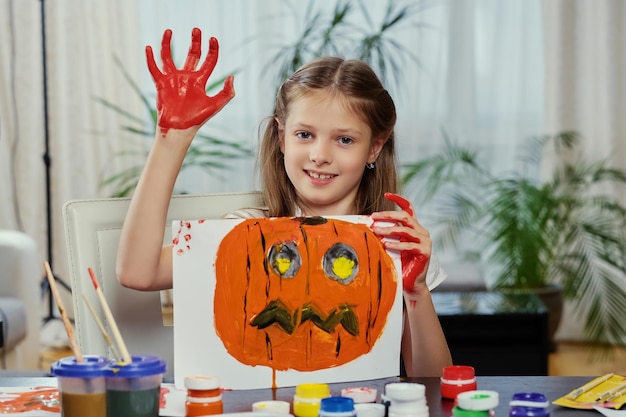 The cute little girl holds a poster with painted Halloween pumpkin.