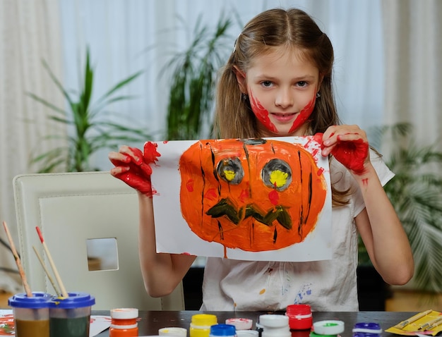 The cute little girl holds a poster with painted Halloween pumpkin.