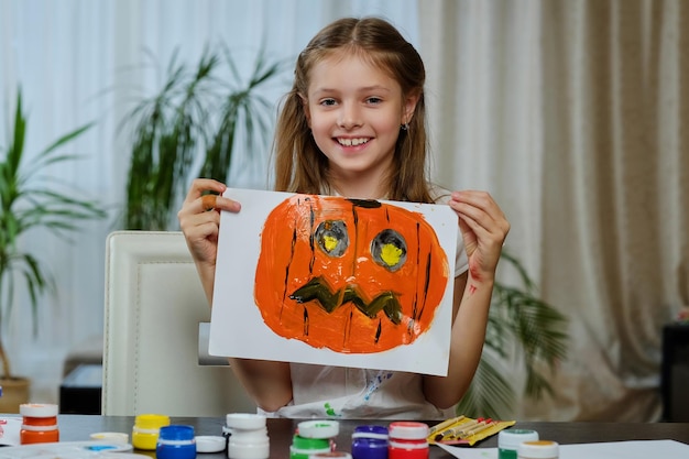 Free photo the cute little girl holds a poster with painted halloween pumpkin.