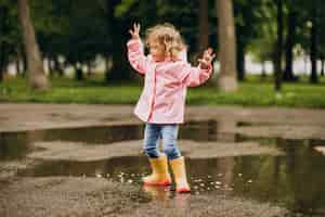 Free photo cute little girl jumping into puddle in a rainy weather