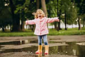 Free photo cute little girl jumping into puddle in a rainy weather