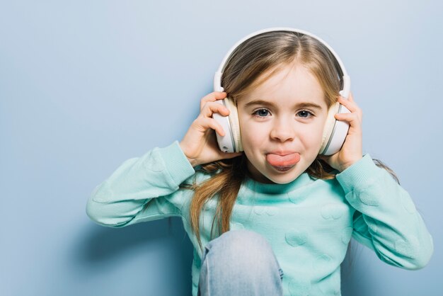 Cute little girl listening music on headphone sticking her tongue out