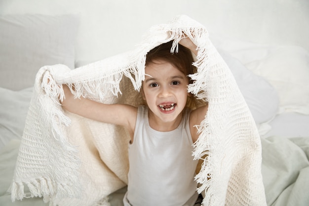 Cute little girl playing in bed with a blanket.